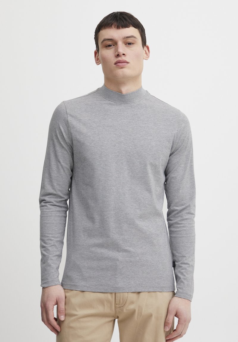 Camisa de manga larga gris claro con cuello alto. Está hecha de una tela suave y elástica. Presenta un corte ajustado y costuras mínimas para un aspecto limpio.