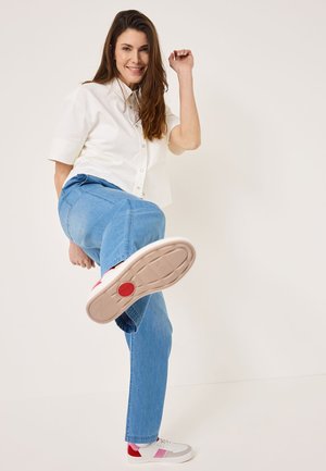 Vit kortärmad skjorta med knappar, ljusblå denimjeans och grå sneakers med röda detaljer, lyft fot som visar souldetaljer.