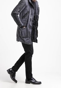 Grå, texturerad parkas med huva, fickor med dragkedja och kontrasterande svarta ärmar. I kombination med slim-fit svarta byxor och blanka svarta skor.