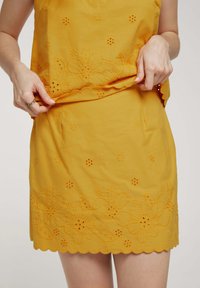 Haut et jupe jaunes brodés présentant des motifs floraux, des détails ajourés et un ourlet festonné. Le tissu semble léger et texturé.