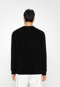 Sudadera negra de manga larga y cuello redondo. Tejido suave, diseño minimalista, puños y dobladillo acanalados. Sin patrones o acentos visibles.