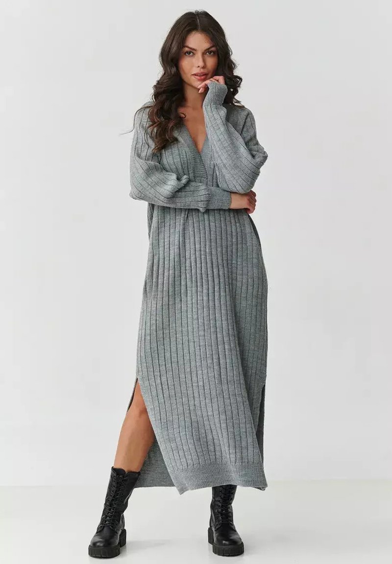 Szara dzianinowa sukienka o pionowej teksturze prążkowanej, z długimi rękawami, głębokim dekoltem w kształcie litery V i bocznymi rozcięciami; w połączeniu z czarnymi botkami na sznurówki.