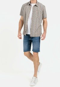 Korte mouwen, gestreepte overhemd in lichte kleuren over een wit T-shirt, gecombineerd met blauwe denim shorts en witte sneakers.