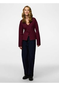 Bugarski kardigan dugih rukava s dubokim V-izrezom i kopčanjem na gumbe, uparen s tamnim širokim trapericama i crnim cipelama.