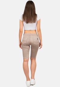 Shorts beiges jusqu'aux genoux en tissu extensible, dotés de deux poches arrière et d'une coupe ajustée. Associés à un top blanc court et à des chaussures blanches.