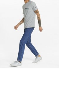 Gray short-sleeve T-shirt with black graphic logo; paired with blue denim jeans and white sneakers with light gray accents.