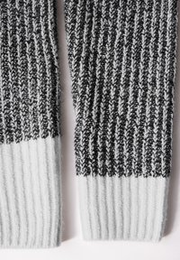Manches de cardigan tricotées dans un motif texturé noir et blanc, avec des poignets côtelés et une section inférieure unie en gris clair.
