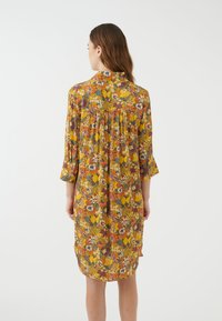 Abito a stampa floreale giallo, con maniche a tre quarti, dettaglio arricciato sul retro e design al ginocchio. Tessuto leggero.