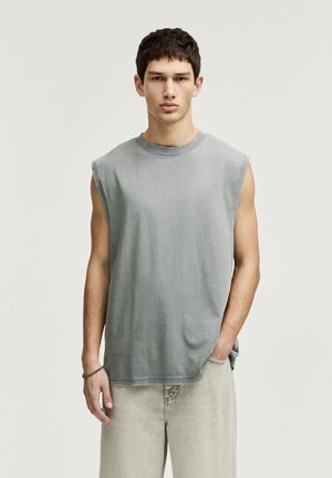Ærmeløs grå bomulds T-shirt med rund hals, afslappet pasform, synlige slidte kanter, parret med lysegrå denim shorts.
