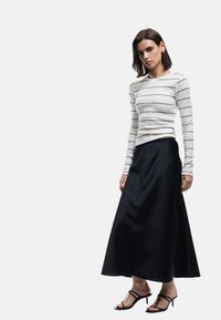 Lang sort nederdel med en glat tekstur, parret med en hvid langærmet top med tynde sorte striber og skulderdetalje. Sorte strappy sandaler.