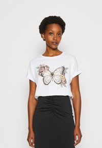 White T-shirt featuring a butterfly and floral graphic in black, pink, and green. Short sleeves, relaxed fit, soft fabric. Black skirt.