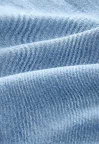 Tejido de mezclilla azul claro con una textura suave y un sutil patrón de sarga, que muestra pliegues y arrugas suaves para un caído natural.