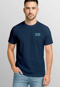 Marineblaue kurzärmelige T-Shirt mit dem „NEVER LESS®“-Logo in hellblau auf der linken Brust. Baumwollmaterial mit einem klassischen Rundhalsausschnitt.