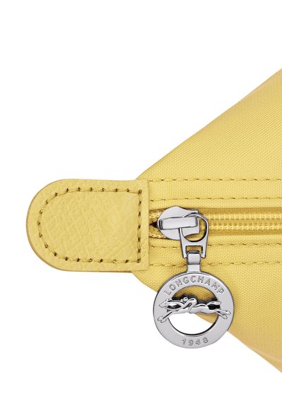 Yellow bag corner with textured leather tab and silver circular Longchamp zipper pull featuring a horse and rider logo.