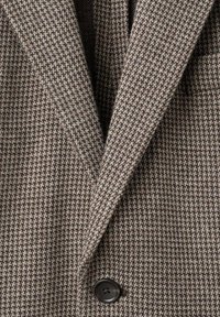 Blazer sartorial in tessuto houndstooth marrone e beige con rever a scatto, dotato di un singolo bottone nero e tessuto strutturato.
