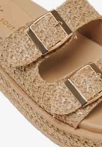 Sandalo platform in paglia intrecciata di colore beige, con due fibbie dorate regolabili sulle cinghie e una parte superiore texturizzata con una soletta liscia.