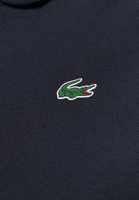 Marineblaue Baumwoll-Polohemd mit strukturiertem Finish, das ein kleines, gesticktes grünes Krokodil-Logo auf der linken Brust zeigt.