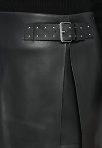 Gonna nera in pelle con cintura larga caratterizzata da dettagli in borchie argentate e una fibbia metallica rettangolare, che mette in risalto una texture liscia e un design pieghettato.