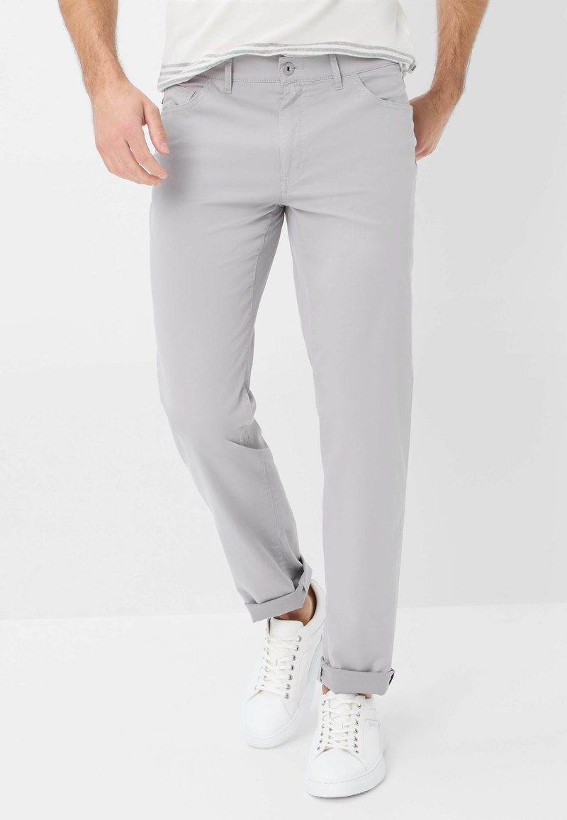Chinos grigi chiaro realizzati in un tessuto misto cotone, con un design a gamba dritta, tasche frontali e orli arrotolati, abbinati a sneakers bianche.