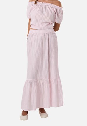 Kvinde iført en lyserød off-shoulder top og matchende lang nederdel med flæsekant, kombineret med hvide flade sko.