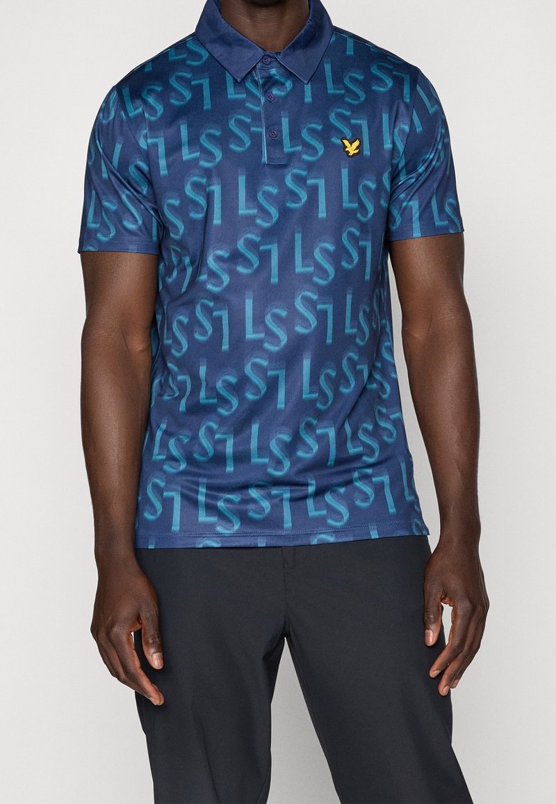 Granatowa koszulka polo o gładkiej fakturze, z powtarzającym się wzorem logo w jasnoniebieskim kolorze i małym żółtym emblematem na lewej piersi.