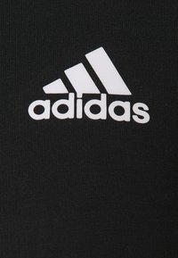 Tissu noir avec une surface texturée présentant un logo Adidas blanc et trois bandes diagonales, indiquant l'identité de la marque.