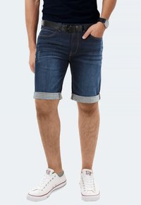 Jeansshorts mit dunkler Wäsche, umgeschlagenen Säumen und slim Fit. Kombiniert mit weißen Sneakers und einem schwarzen Gürtel, der einen lässigen Stil zeigt.