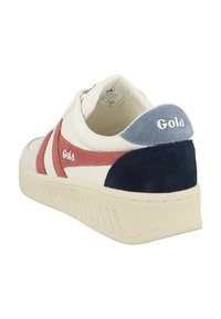 Baskets blanches avec des accents en daim rouge et marine, semelle texturée, logo Gola au niveau du talon, et tige en cuir lisse avec des éléments de design contrastants.