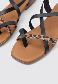 Sandalias planas con correas de cuero negro y un acento de estampado de leopardo. Diseño de punta cuadrada con una plantilla suave en tono marrón claro y hardware minimalista.