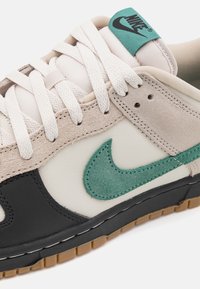 Nike Dunk tenisice s mješavinom kreme kože, crne kože i bež antilopa, s teksturiranim zelenim Swoosh logoom i bijelim vezicama.