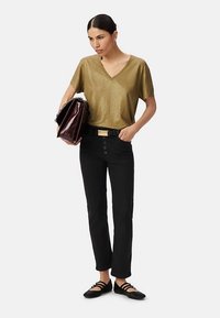 Gouden metallic top met korte mouwen en V-hals, zwarte aangesloten broek met knoopdetails, zwarte ballerina's en een bordeauxrode handtas.