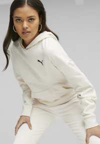 Felpa crema con tasca a canguro, con un logo Puma nero sul petto. Tessuto morbido, maniche lunghe, vestibilità rilassata. Abbinata a pantaloni coordinati.