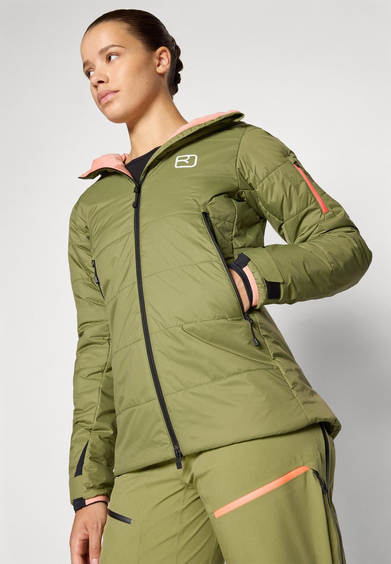 Grüne isolierte Jacke mit pinkem Futter in der Kapuze, mit Reißverschlusstaschen und schwarzen Bündchen. Verfügt über ein Logo auf der Brust und kontrastierende Reißverschlussakzente.