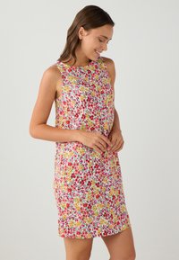 Bloemenjurk met een mouwloos ontwerp, met een kleurrijk patroon van kleine bloemen op een lichte achtergrond. Soepele stof en kniehoogte.