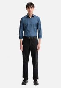 Camicia blu con bottoni e maniche lunghe, abbinata a pantaloni neri e scarpe nere, caratterizzata da una texture liscia e un design aderente.