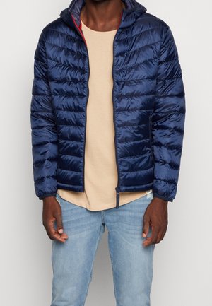 Marineblaue Steppjacke mit glatter, ge quilteter Textur und Kapuze, verziert mit einem roten Akzent entlang des Reißverschlusses und taillierter Passform.
