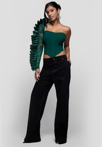 Vihreä, yhden olkapään bodysuit, jossa on pitsi- ja röyhelöhihat, yhdistetty korkeavyötäröisiin, leveälahkeisiin mustiin farkkuihin.