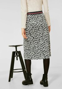 Mustat ja valkoiset kuviolliset hameet kapenevalla designilla, joustovyötärö, jossa on punaisia yksityiskohtia, yhdistettynä mustiin legginsseihin ja paksupohjaisiin saappaisiin.