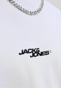 Balta medvilnė marškinėliai su juodu "JACK & JONES" logotipu. Papuošti sidabriniu grandinės kaklo papuošalu, pabrėžiančiu kasdienį dizainą.