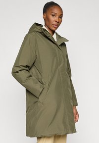 Olivově zelený voděodolný parka s kapucí, zapínání na zip, boční kapsy a nastavitelné pas. Hladká textura, dlouhá do kolen.