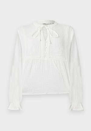 Blouse blanche à manches longues avec tissu texturé, motifs floraux brodés, patte de boutonnage et détail de nouage au col.