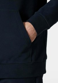 Felpa di colore blu scuro con tasca a kangaroo, polsi e orlo a coste, e un tessuto morbido e testurizzato. Design minimalista senza motivi.