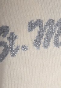 Tessuto a maglia color crema con scritte grigio argento parzialmente visibili, impreziosito da piccole perline argentate lucide.