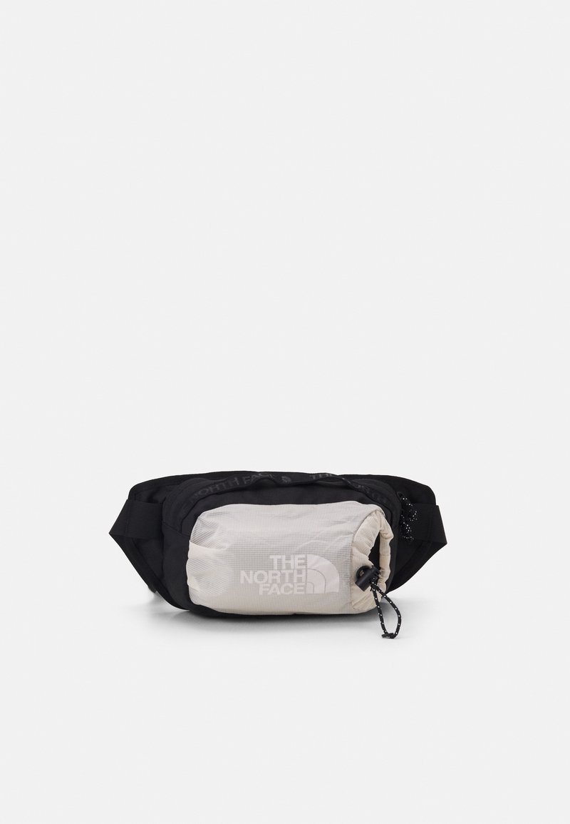 Banane noire avec poche avant gris clair, fermeture éclair et logo The North Face sur le devant, sur fond blanc uni.