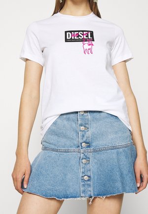 Femme portant un t-shirt blanc avec un logo Diesel noir et un croquis de chat rose, associé à une jupe en denim bleu clair à boutons.
