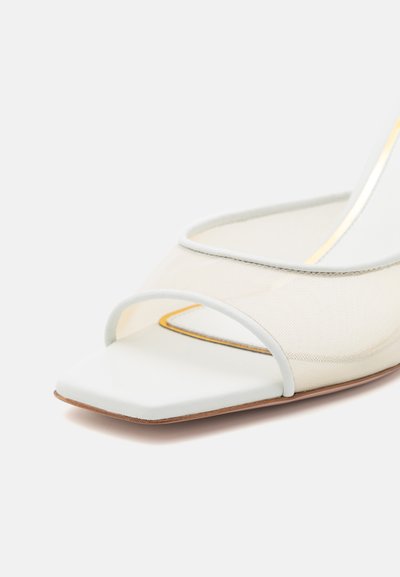 Zapato abierto de malla transparente con un diseño de punta cuadrada, detalles en cuero blanco y una suela de goma marrón con un sutil ribete dorado.