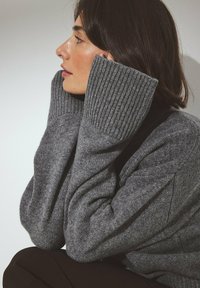 Gray knitted sweater with ribbed cuffs. The fabric appears thick and textured, adding warmth to the overall design.