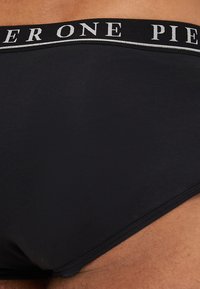 Schwarze Baumwollslips mit breitem elastischen Bund, der den Text "PIER ONE" in Weiß trägt. Glatte Textur und enganliegendes Design für hohen Komfort.