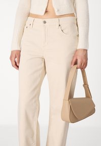 Jeans beige a vita alta con taglio dritto e tasche frontali, abbinati a una piccola borsa in pelle color tan con forma strutturata e tracolla regolabile.