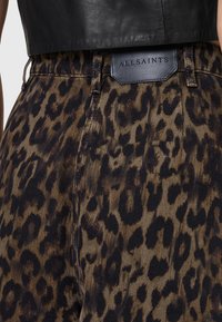 Traperice s leopard uzorkom s teksturiranom površinom, smešnim i crnim uzorkom, te kožnom oznakom AllSaints na struku.